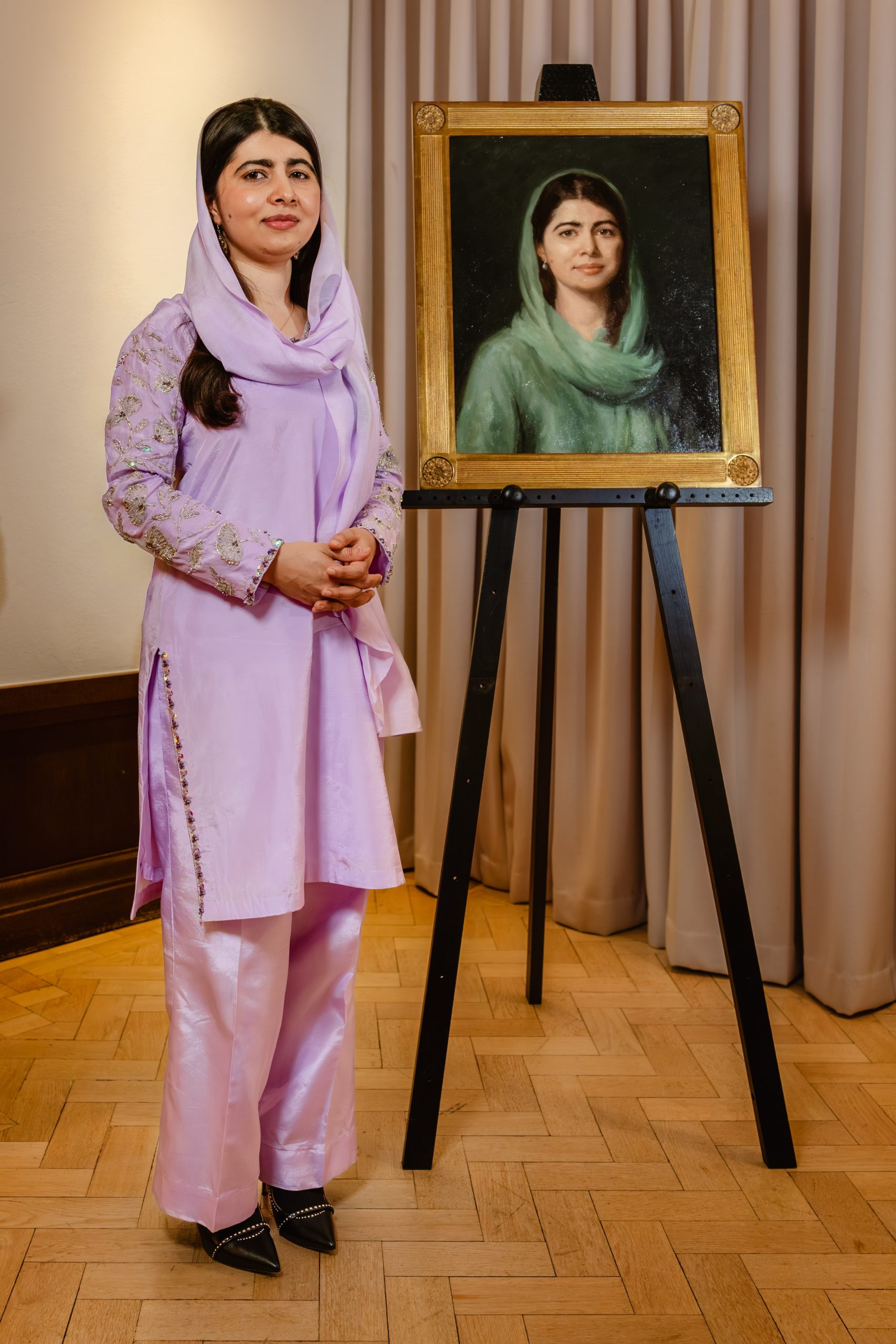 Malala Yousafzai standing beside her newly unveiled portrait at Lady Margaret Hall in Oxford.